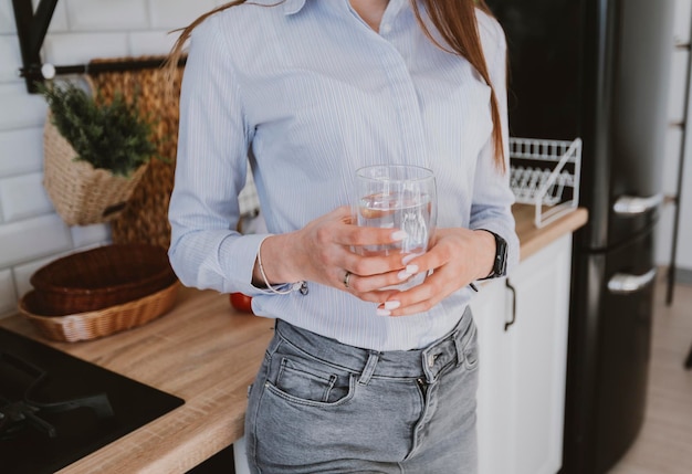 a young girl stands in the kitchen holding a glass of clean water