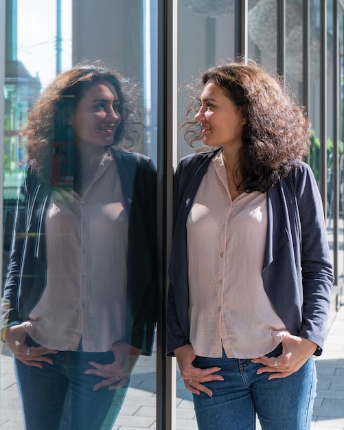 A young girl stands near a large window and looks at her reflection