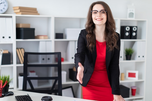 A young girl stands in the office near the table and stretches her hand forward