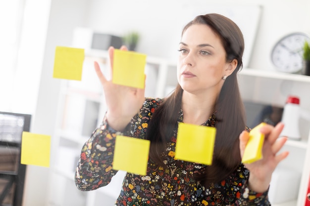 A young girl stands in the office near a transparent Board with stickers.