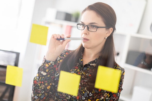 A young girl stands in the office near a transparent Board with stickers.