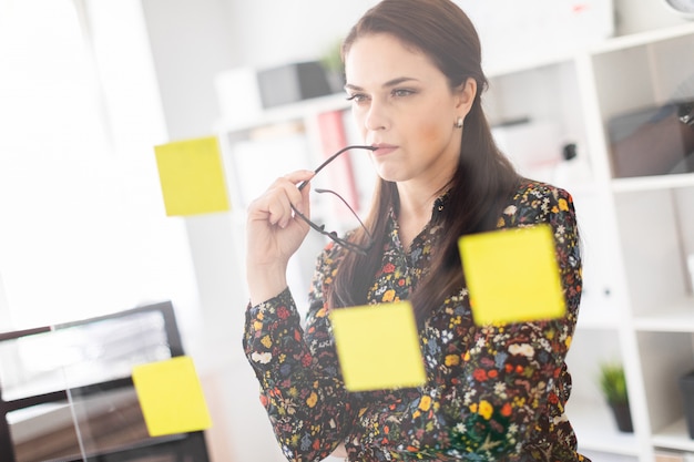 A young girl stands in the office near a transparent Board with stickers.