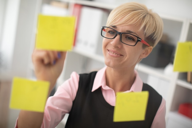 A young girl stands in the office near a transparent Board with stickers.