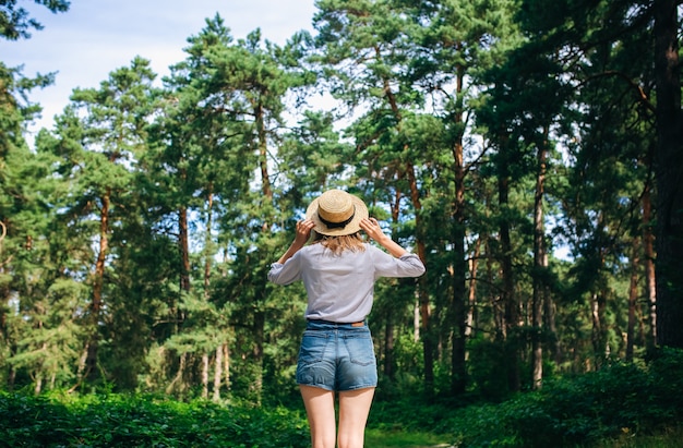 young girl in straw hat standing in the forest