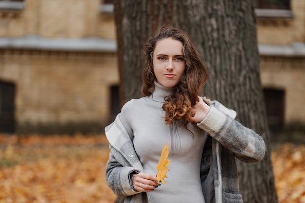 Young girl student in a gray coat talking by phone of the university background