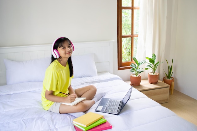 Young girl studying with laptop on bed in bedroom