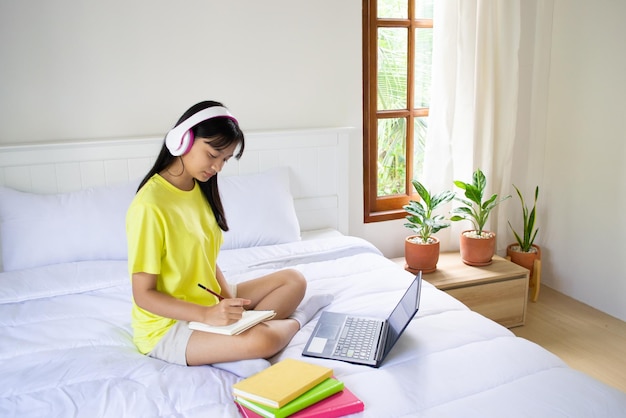 Young girl studying with laptop on bed in bedroom