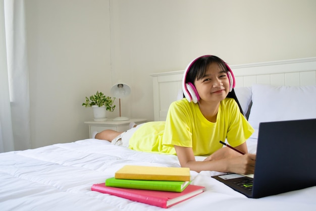 Young girl studying with laptop on bed in bedroom