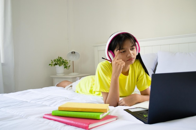 Young girl studying with laptop on bed in bedroom