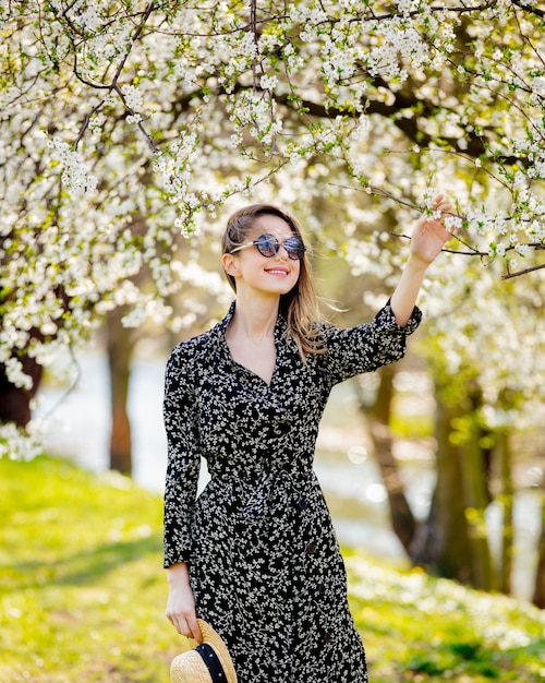 Young girl in a sunglasses and hat stay near a flowering tree in the park. Spring season