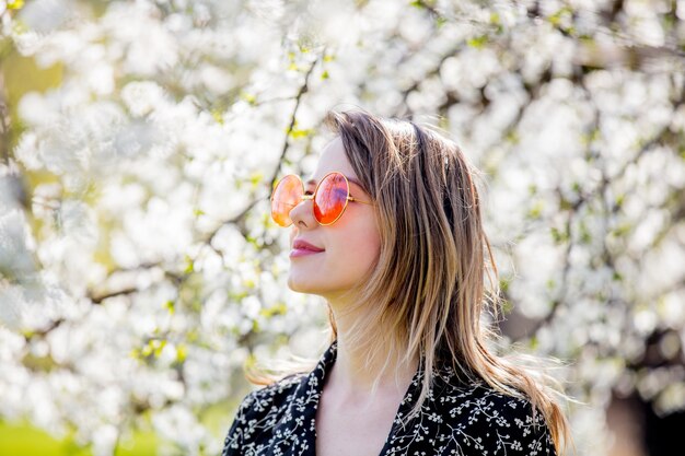 Young girl in a sunglasses stay near a flowering tree in the park. Spring season