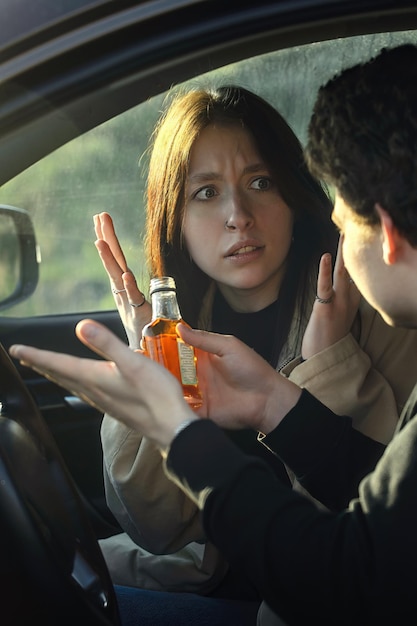 Photo a young girl takes away a bottle of alcohol from her boyfriend while driving a car