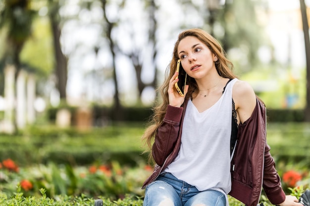 Young girl talking with her smartphone sitting on a bench in the park format with copy space close up