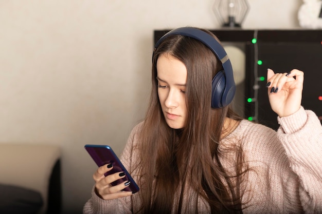 Young girl teen student listens to music at home with headphones from smartphone