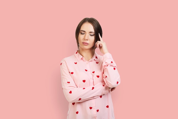 The young girl thought holding a finger in the wax Isolated on pink background in a pink shirt with red hearts