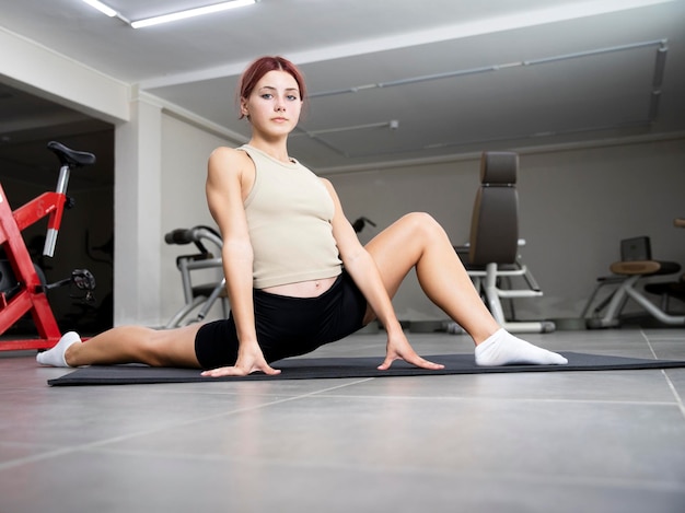 A young girl trains in the gym The gymnast sits in the twine on the mat Leg stretch