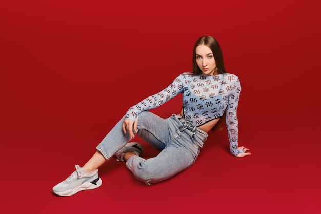 Young girl in transparent top and jeans sits on the floor in red background