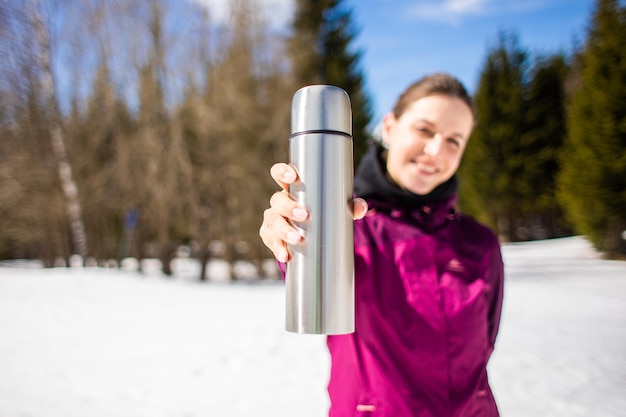 A young girl traveler is holding thermos against the background of mountains and snow