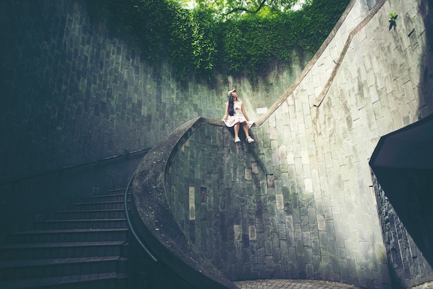 Young girl traveler sitting on circle stairs of a spiral staircase of an underground cross