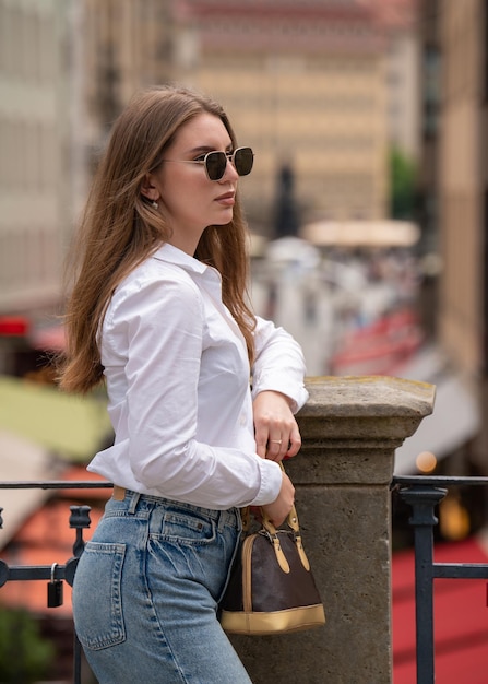 A young girl travels and visits different cities Standing with a small bag in his hands looking into the distance Caucasian model with long hair and sunglasses