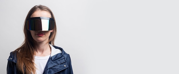 Young girl in virtual reality glasses in a blue jacket on a light background. Banner.