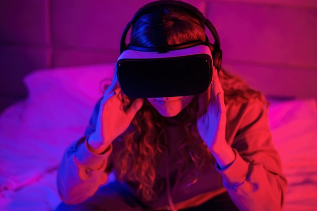 Young girl in virtual reality glasses with blue and red illumination in the room In the bed. Entertainment at home