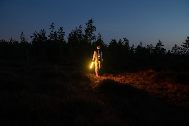 Young girl walk countryside at night hold led lamp to highlight pathway to camp or car after hiking