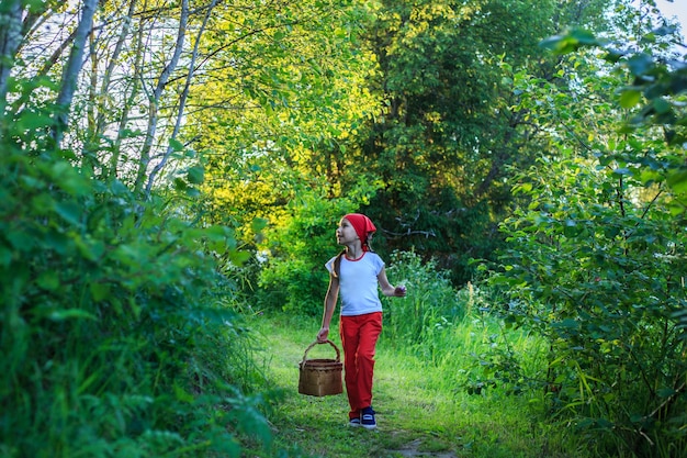 Young girl walking on a path through green woods carrying a birchbark basket