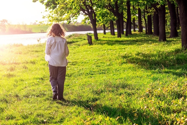 A young girl walks along a forest road near a river in sunny summer weather A walk in the forest