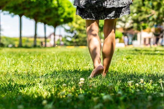 A young girl walks barefoot on a green lawn Back view