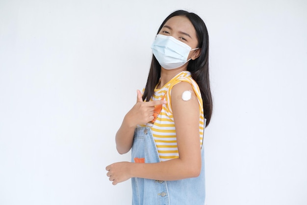 Young girl wear mask showing arm after vaccination on white background.