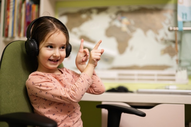 Young girl wearing headphones enjoys her remote education Distant studying homeschooling Show fingers up