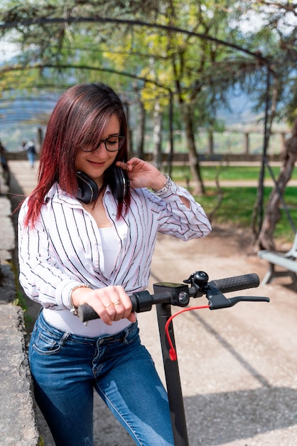 Young girl wearing a shirt and headphones and riding a e-scooter in a park