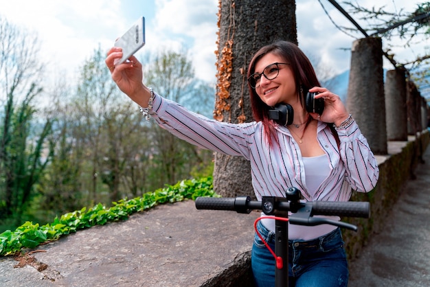 Young girl wearing a shirt and headphones taking a selfie riding a scooter