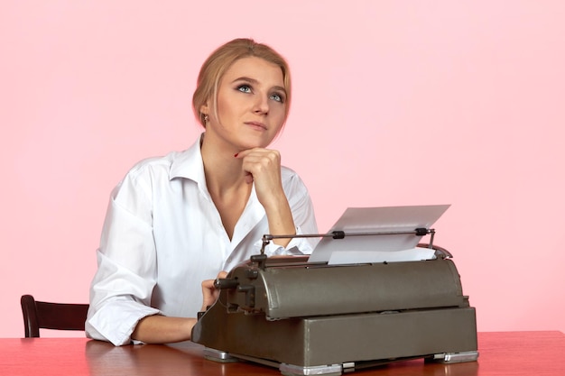 A young girl in a white blouse sits at a desk in the office and types text on a retro typewriter.