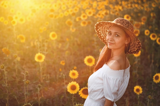 A young girl in a white dress and hat in a field of sunflowers at sunset Portrait of a woman with a slim figure on a background of yellow flowers