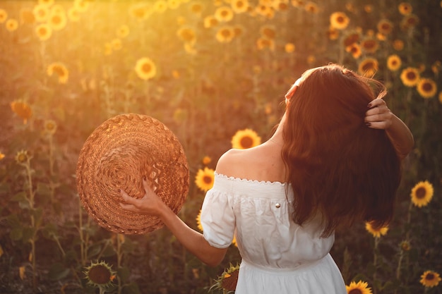 A young girl in a white dress and hat in a field of sunflowers at sunset Portrait of a woman with a slim figure on a background of yellow flowers