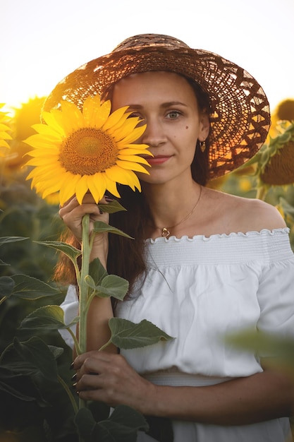 A young girl in a white dress and hat in a field of sunflowers at sunset Portrait of a woman with a slim figure on a background of yellow flowers