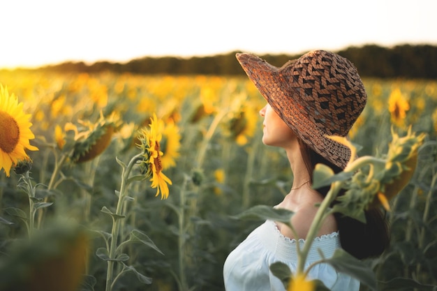 A young girl in a white dress and hat in a field of sunflowers at sunset Portrait of a woman with a slim figure on a background of yellow flowers