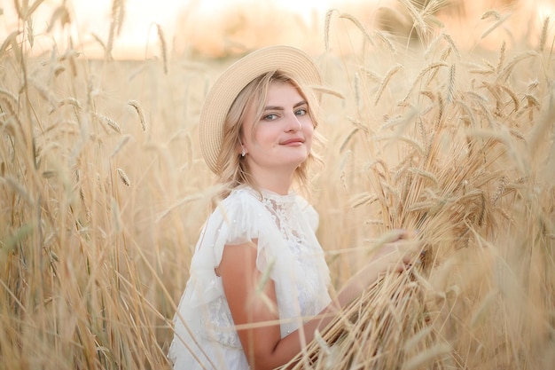 A young girl in a white dress in yellow wheat in the summer at sunset