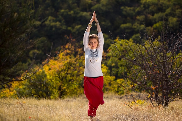 Young girl in a white shirt and red pants doing yoga outdoors