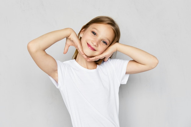 Young girl in white t-shirt holds palm of her hands near cheeks