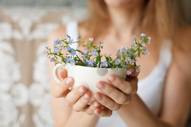 Young girl in a white tank holding a dotted cup with forgetmenot Flowers in a mug Hands with flowers