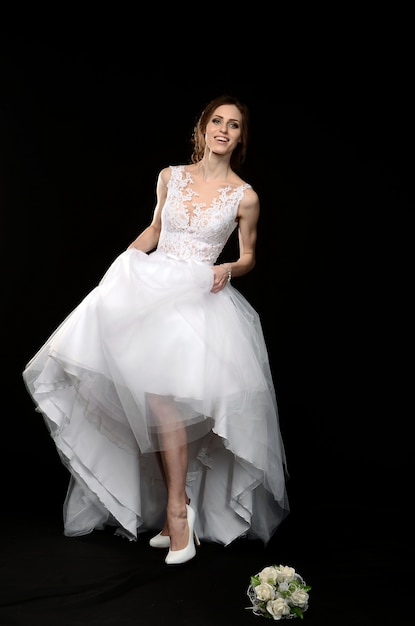 Young girl in white in a wedding dress barefoot, emotional happy mysterious bride on a black background.