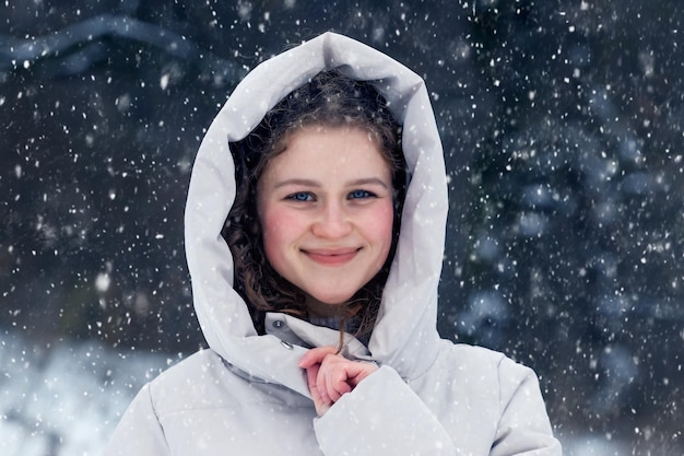 Young girl in the winter forest during a snowfall. Portrait of a young happy girl in the winter forest