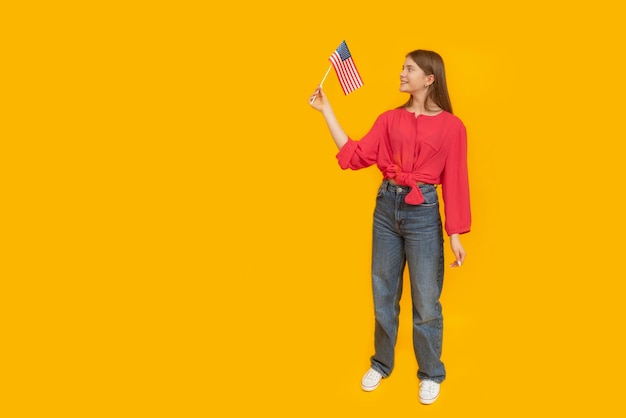 Young girl with an American flag in her hands Fulllength portrait of teenager on yellow background Space for text