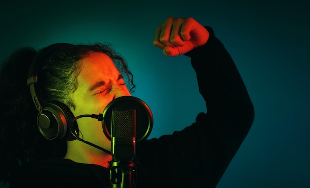 Young girl with an arm raised and her eyes closed while she39s singing with headphones and a microphone indoors with copy space