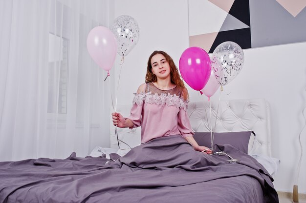 Young girl with balloons on bed posed