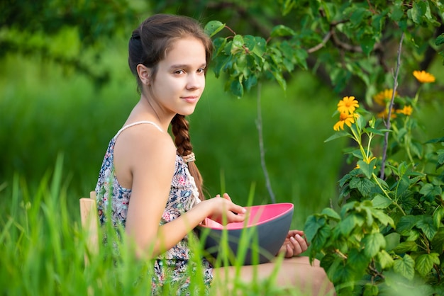 Young girl with a brown braid picks fresh berries from a large bush