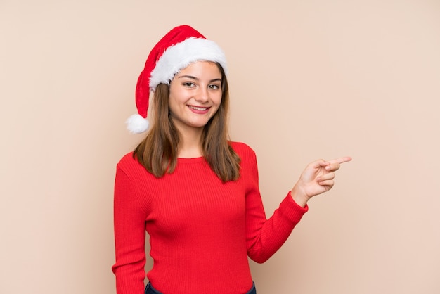 Young girl with christmas hat over isolated background pointing finger to the side